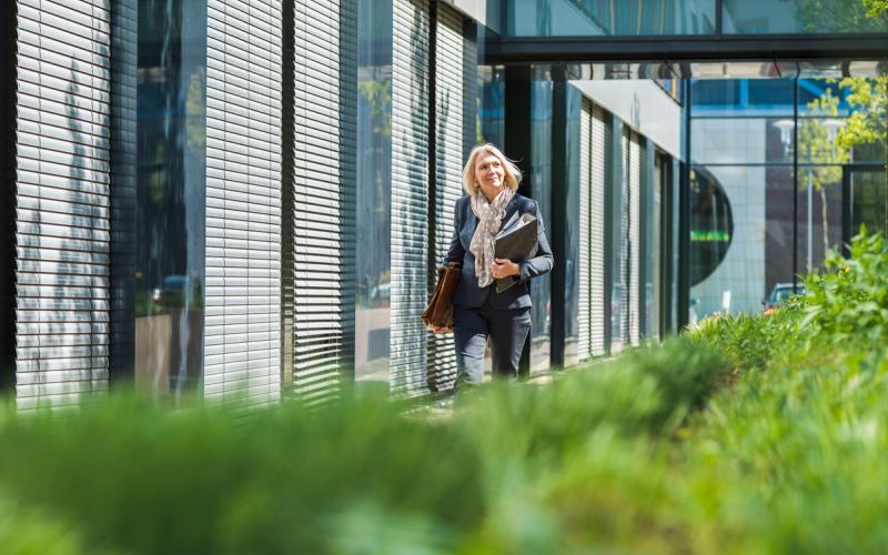 Frau mit Laptop und Unterlagen neben Immobilie grün